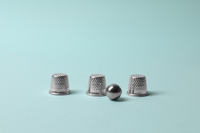 Photo of Metal thimbles and ball on light blue background. Thimblerig game