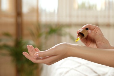 Photo of Young woman applying essential oil onto wrist indoors, closeup