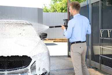 Businessman cleaning auto with high pressure water jet at self-service car wash