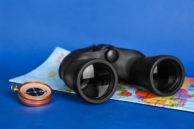 Photo of Modern binoculars, compass and map on blue background, closeup