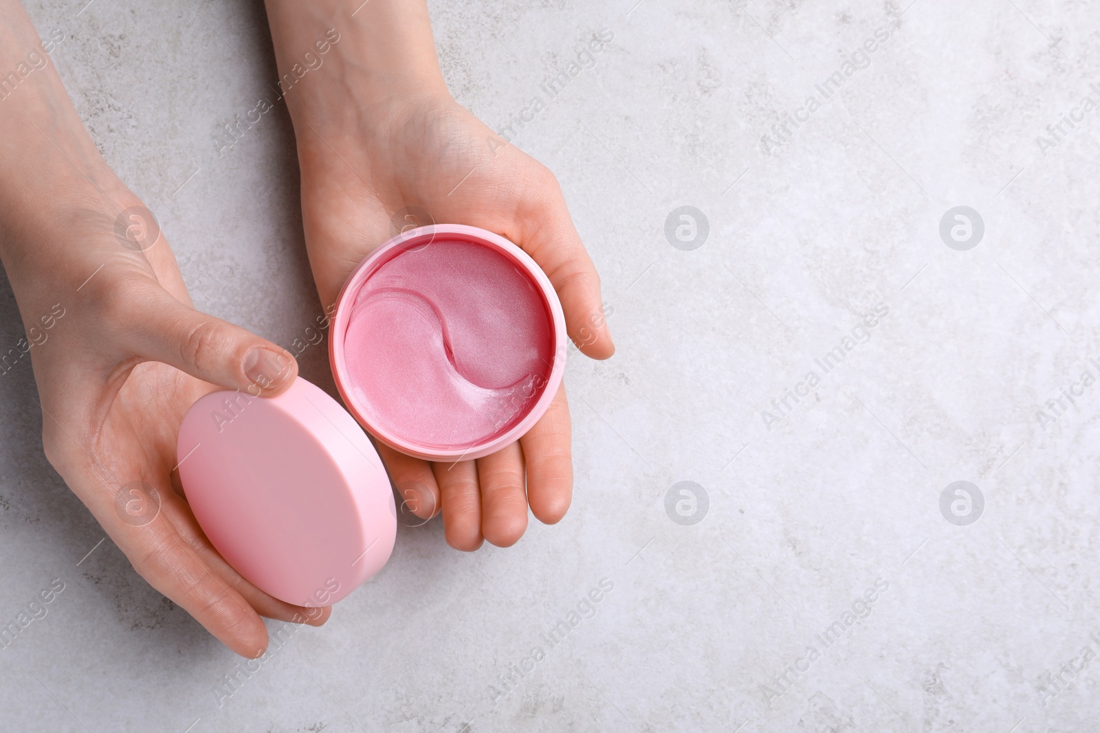 Photo of Woman holding package of under eye patches at light table, top view with space for text. Cosmetic product