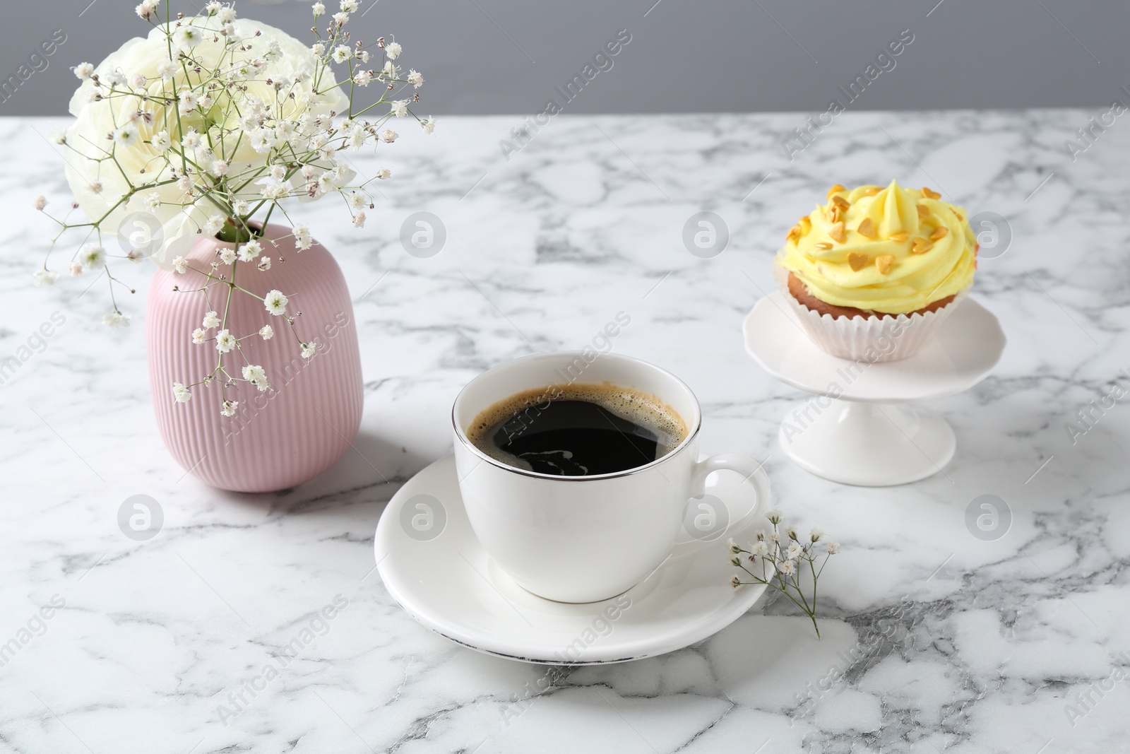 Photo of Delicious cupcake with yellow cream, coffee and flowers on white marble table