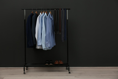 Rack with stylish clothes near black wall