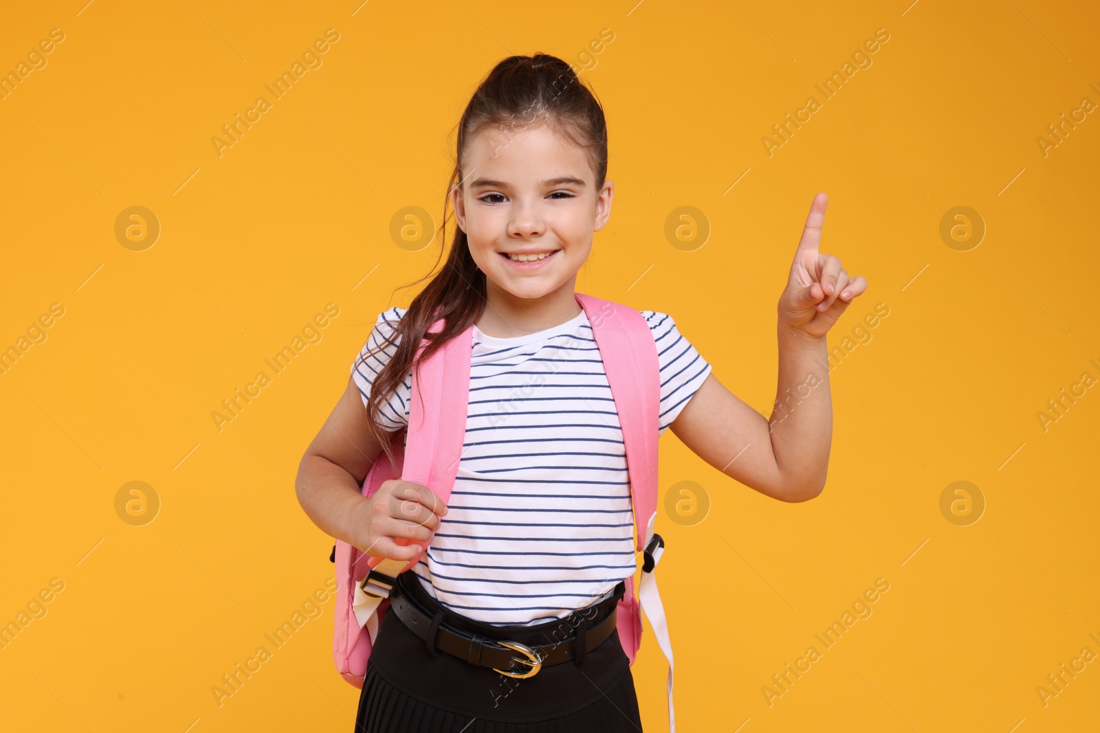 Photo of Cute schoolgirl pointing upwards on orange background