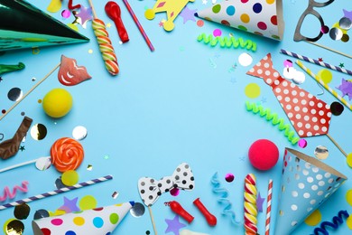 Photo of Frame of party hats and other festive items on light blue background, flat lay with space for text. Birthday surprise