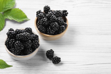 Photo of Ripe blackberries and green leaves on white wooden table, space for text