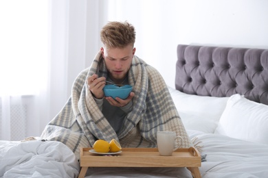 Photo of Sick young man eating soup to cure flu in bed at home