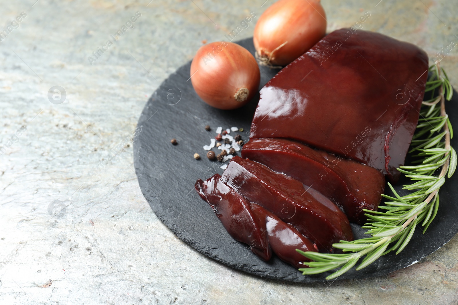 Photo of Cut raw beef liver with rosemary and onions on grey table, closeup. Space for text