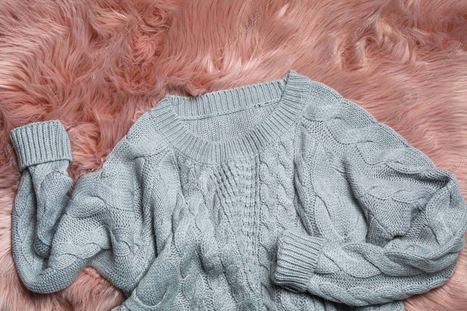 Photo of Grey knitted sweater on pink fur rug, flat lay
