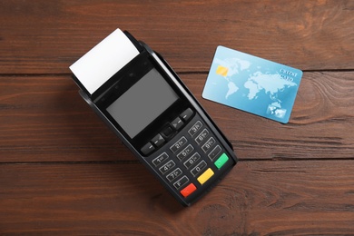 Photo of Modern payment terminal and credit card on wooden background, top view