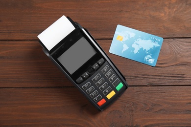 Modern payment terminal and credit card on wooden background, top view