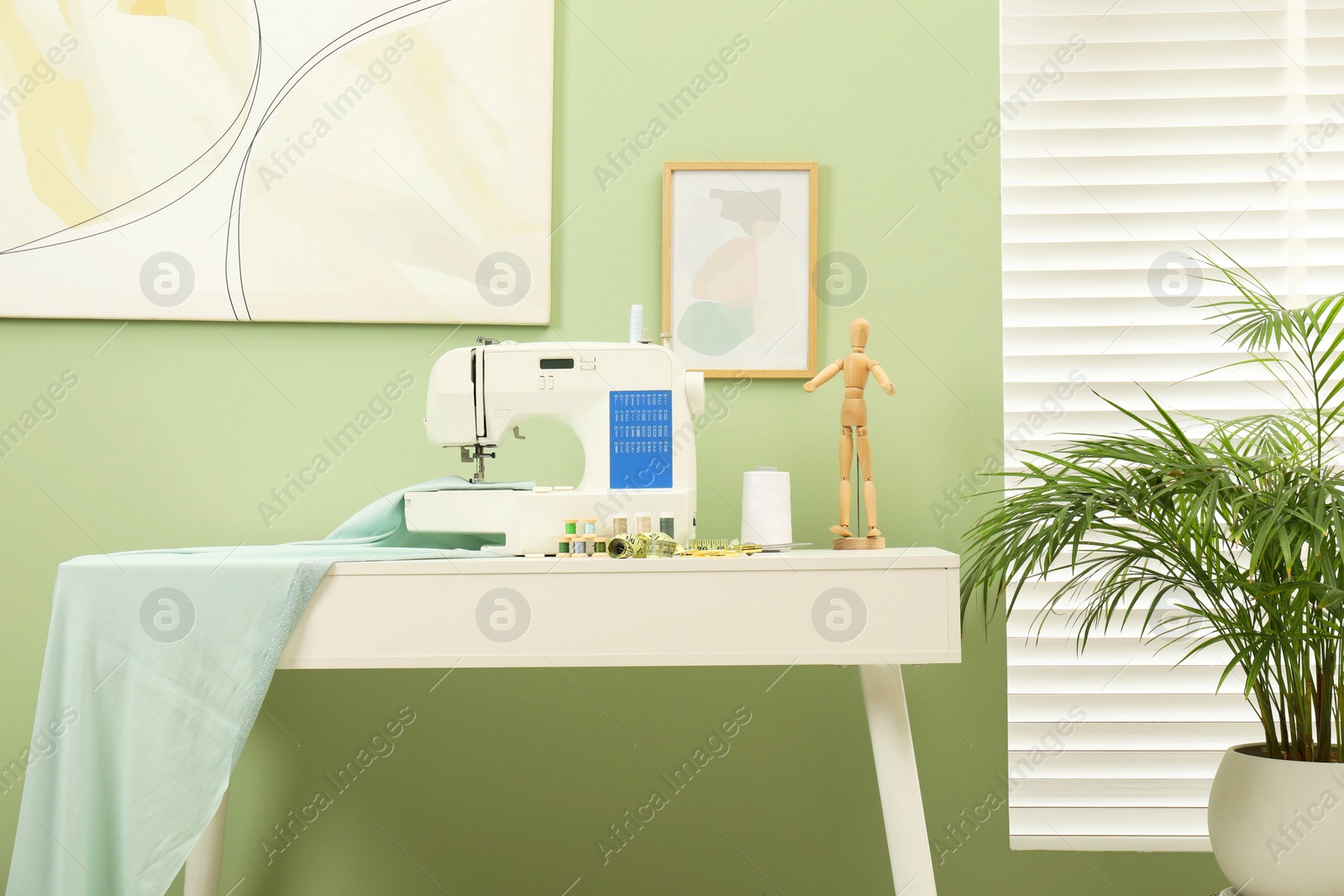 Photo of Modern sewing machine with cloth and craft accessories on white table near window in room