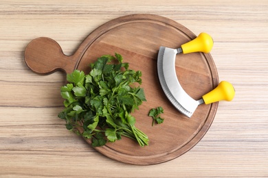 Composition with mezzaluna knife and bunch of parsley on wooden table, top view. Clean dishes