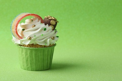 St. Patrick's day party. Tasty cupcake with sour rainbow belt and pot of gold toppers on green background. Space for text