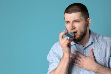 Young man using asthma inhaler on color background with space for text