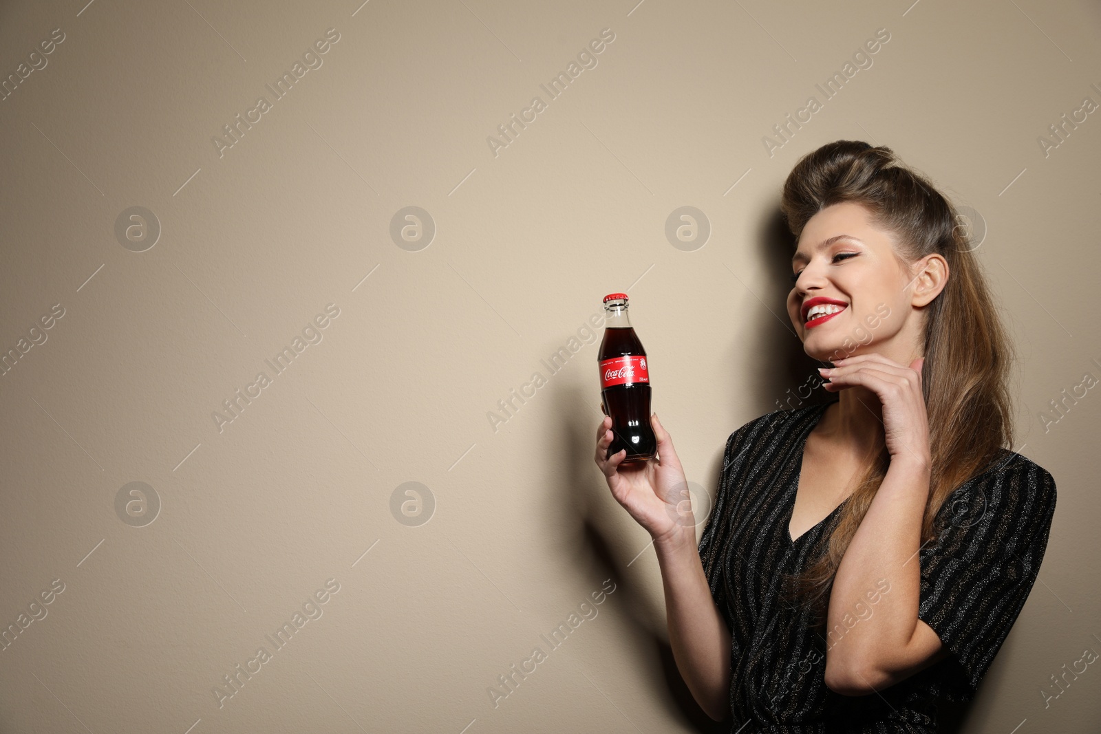 Photo of MYKOLAIV, UKRAINE - NOVEMBER 28, 2018: Young woman with bottle of Coca-Cola on color background, space for text