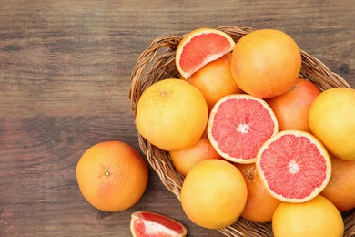 Photo of Wicker basket with fresh grapefruits on wooden table, flat lay
