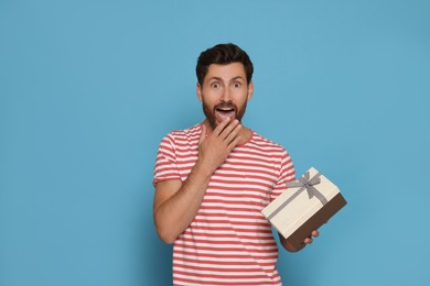 Photo of Emotional man holding gift box on turquoise background
