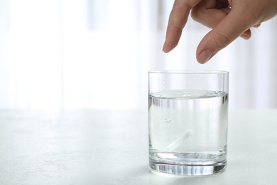 Photo of Woman putting tablet into glass of water indoors, space for text