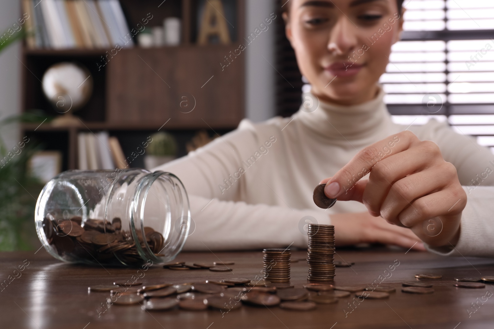 Photo of Woman stacking coins at wooden table indoors, closeup