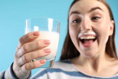 Photo of Emotional woman with milk mustache holding glass of tasty dairy drink on light blue background, selective focus