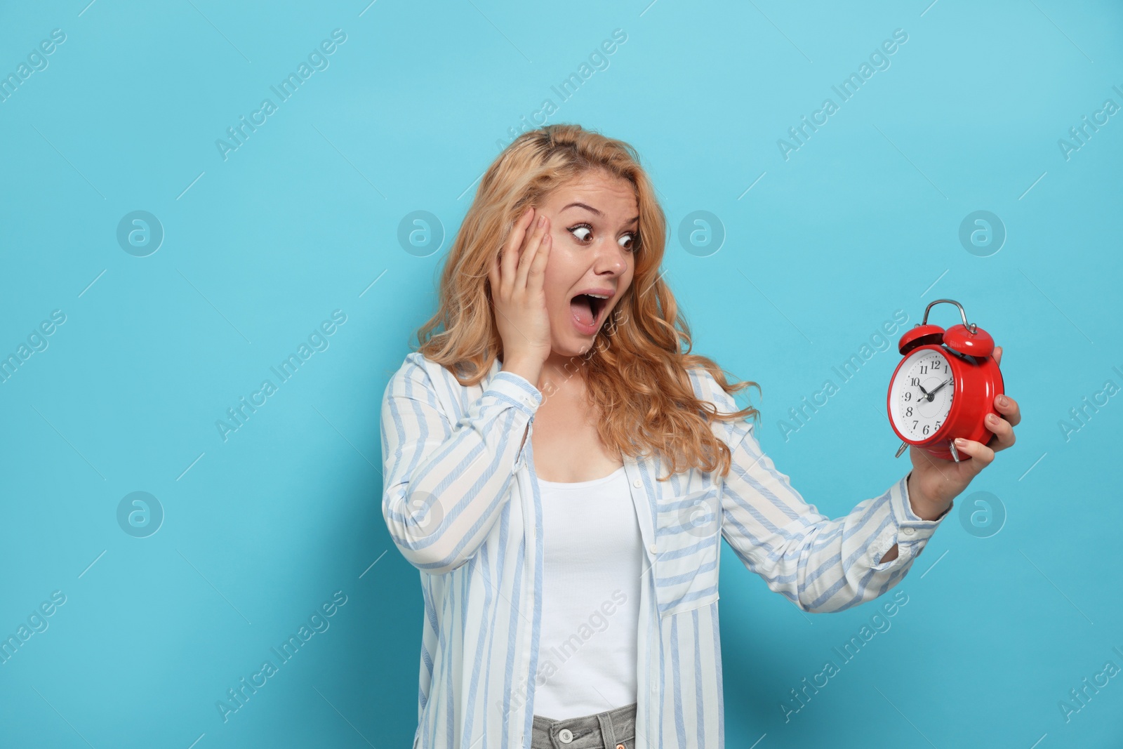 Photo of Emotional woman with alarm clock in turmoil over being late on light blue background