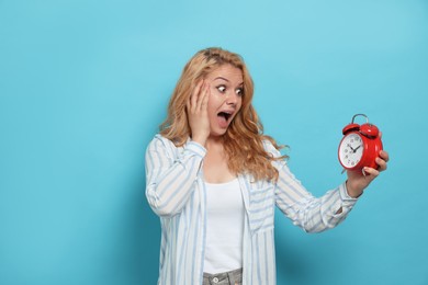 Emotional woman with alarm clock in turmoil over being late on light blue background