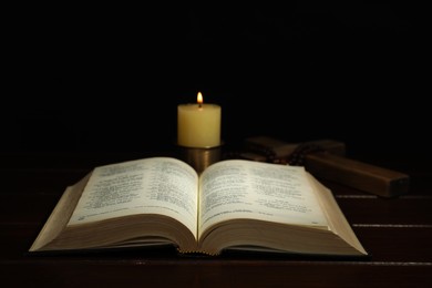 Photo of Church candle, Bible, cross and rosary beads on wooden table