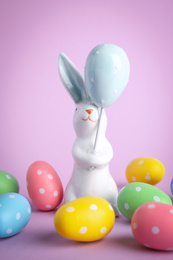 Easter bunny figure and dyed eggs on violet background