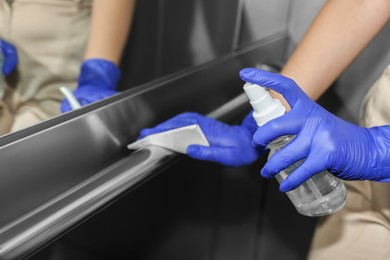 Photo of Woman wiping elevator`s handrails with detergent, closeup