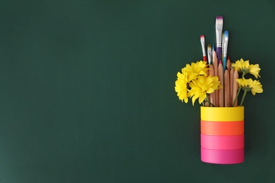 Different school stationery and beautiful yellow flowers on green chalkboard, flat lay with space for text. Happy Teacher's Day