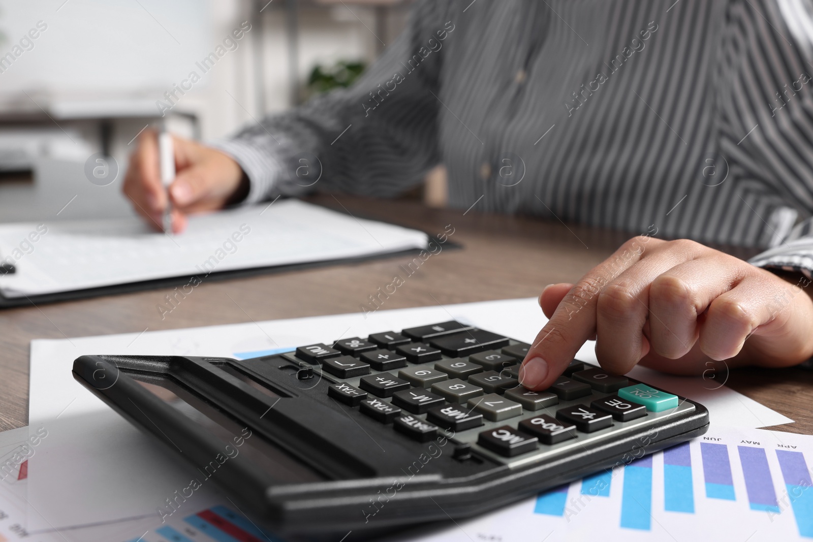 Photo of Woman using calculator while taking notes at table indoors, closeup