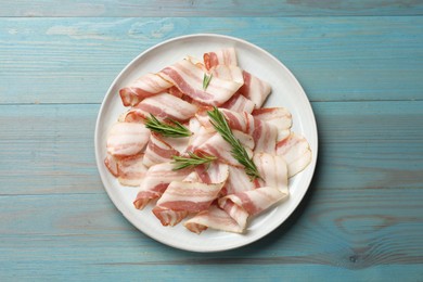 Slices of raw bacon and rosemary on light blue wooden table, top view