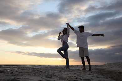 Happy couple dancing on beach at sunset