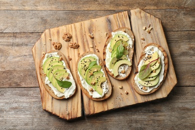 Photo of Board with avocado bruschettas on wooden table, flat lay