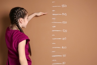 Photo of Little girl measuring her height on color background