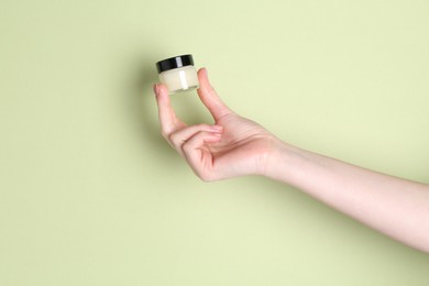 Woman holding jar of cream on green background, closeup