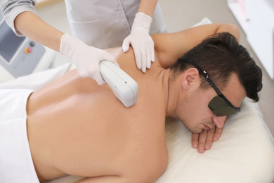 Photo of Young man undergoing laser epilation procedure in beauty salon