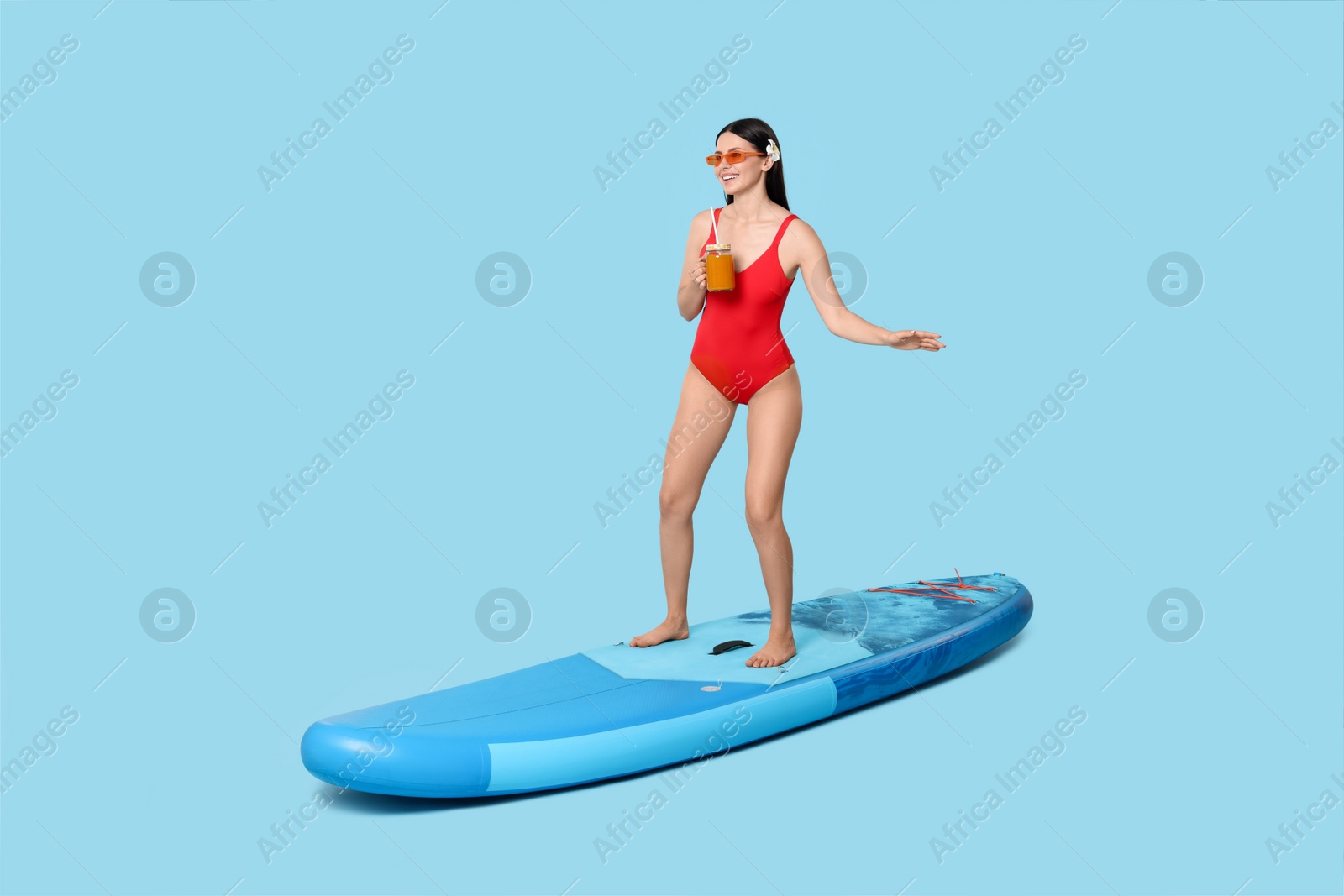 Photo of Happy woman with refreshing drink on SUP board against light blue background