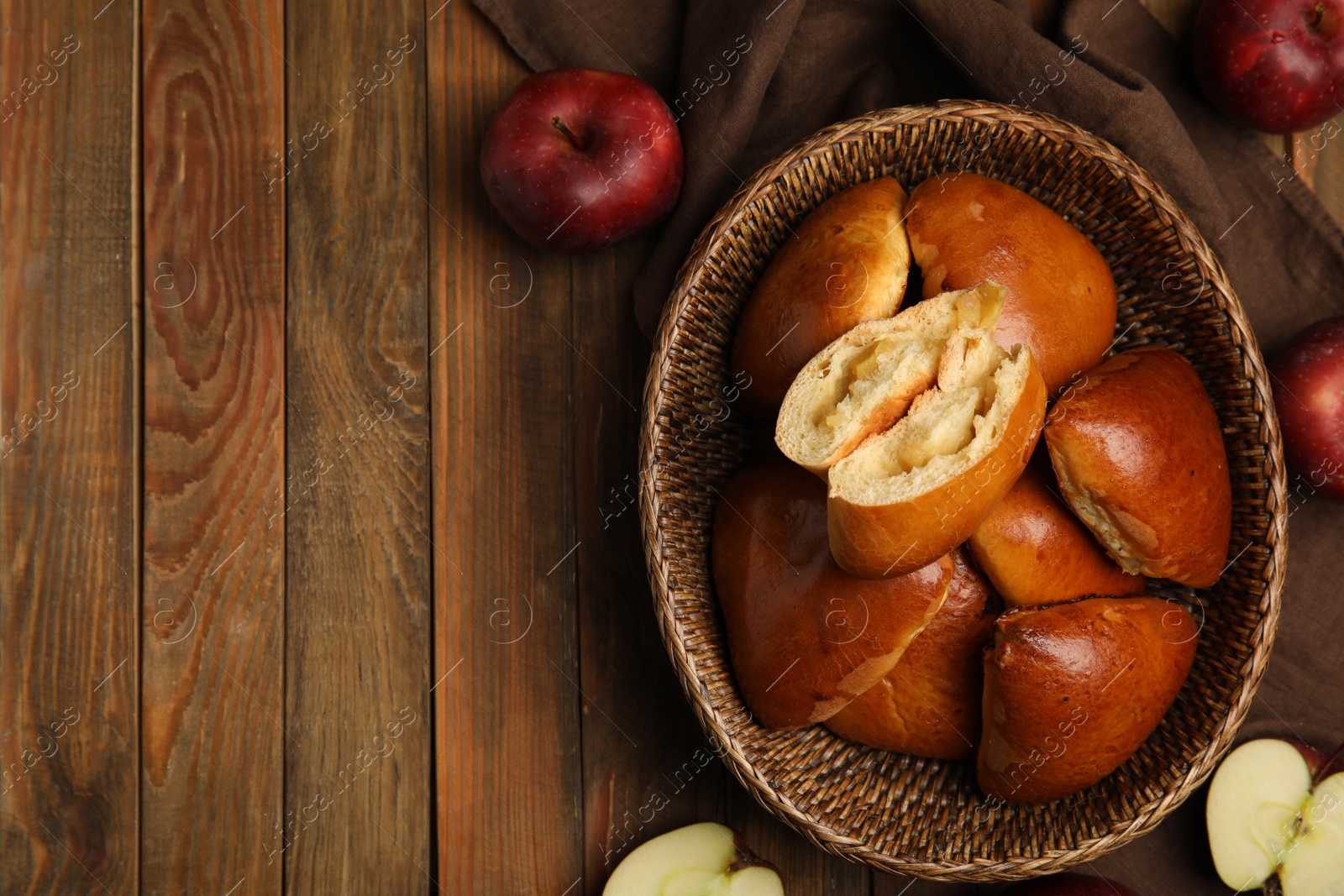 Photo of Delicious baked apple pirozhki in wicker basket and fruits on wooden table, flat lay. Space for text