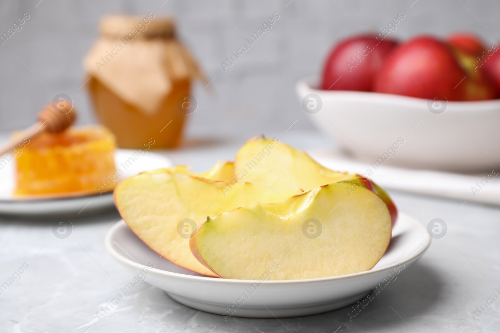 Photo of Apple slices near honey on light grey marble table, closeup. Rosh Hashanah holiday