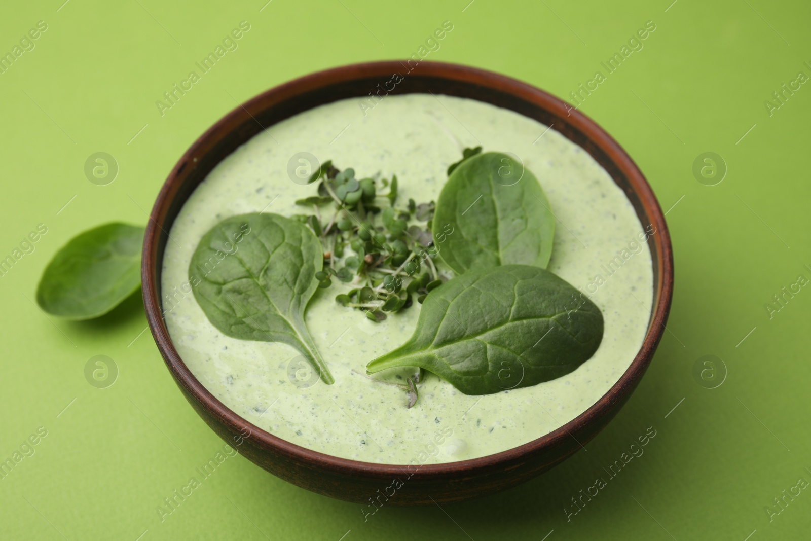 Photo of Delicious spinach cream soup with fresh leaves and microgreens in bowl on green background