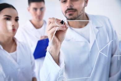 Photo of Medical students writing chemical formula on glass whiteboard in laboratory