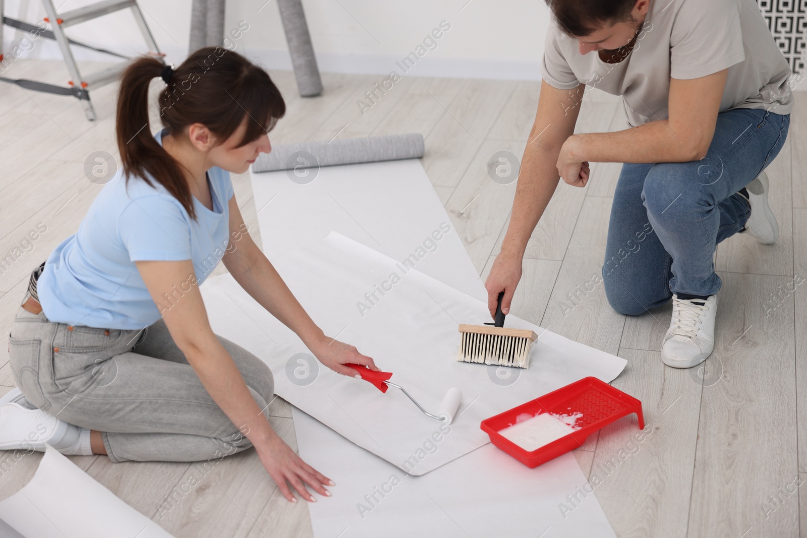 Photo of Couple applying glue onto wallpaper sheet in room