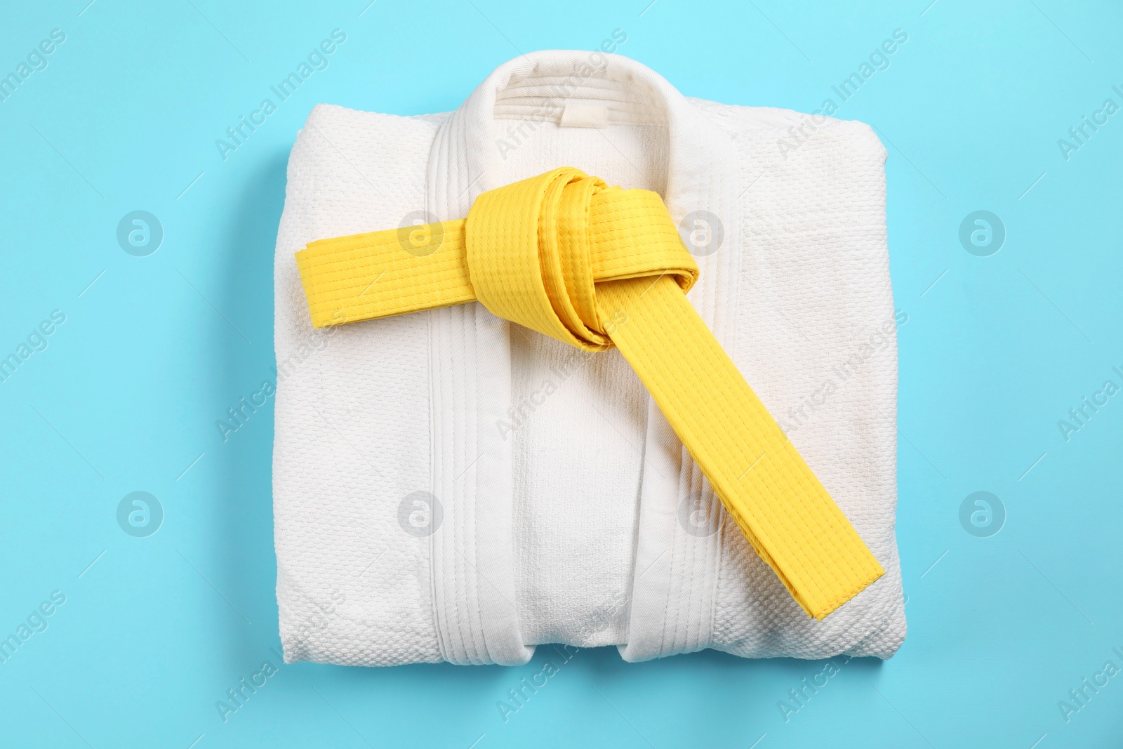 Photo of Yellow karate belt and white kimono on light blue background, top view