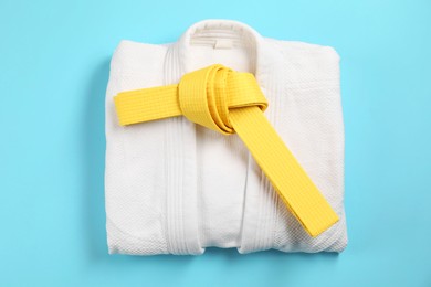 Photo of Yellow karate belt and white kimono on light blue background, top view