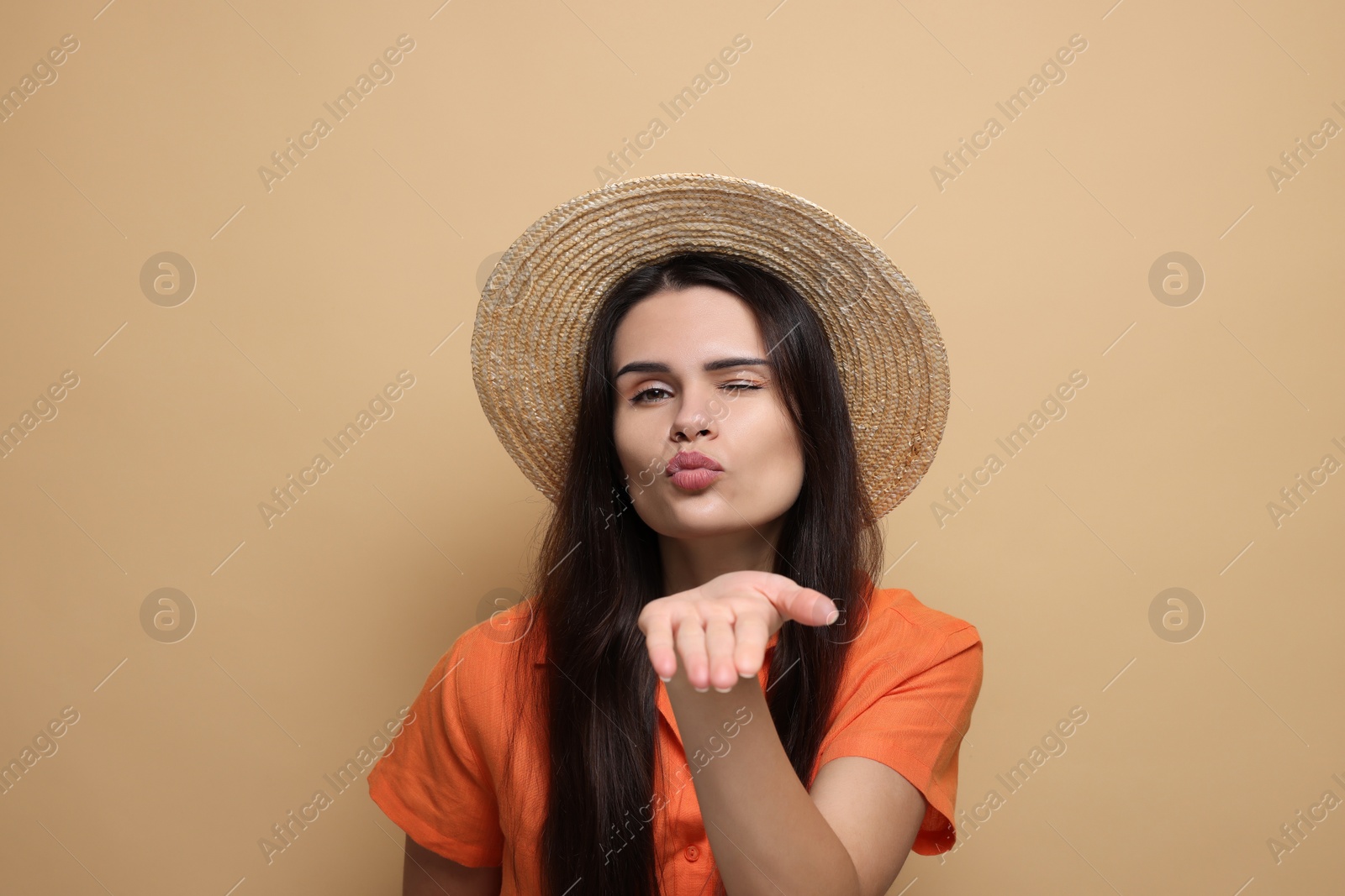 Photo of Beautiful young woman in straw hat blowing kiss on beige background