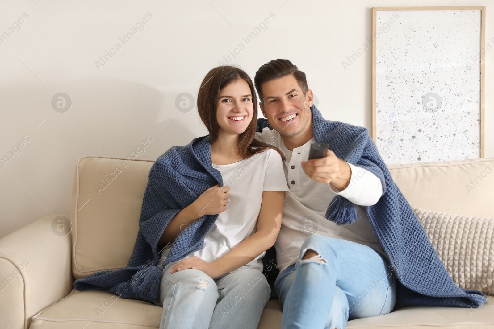 Photo of Happy couple covered with warm dark blue plaid watching television on sofa at home