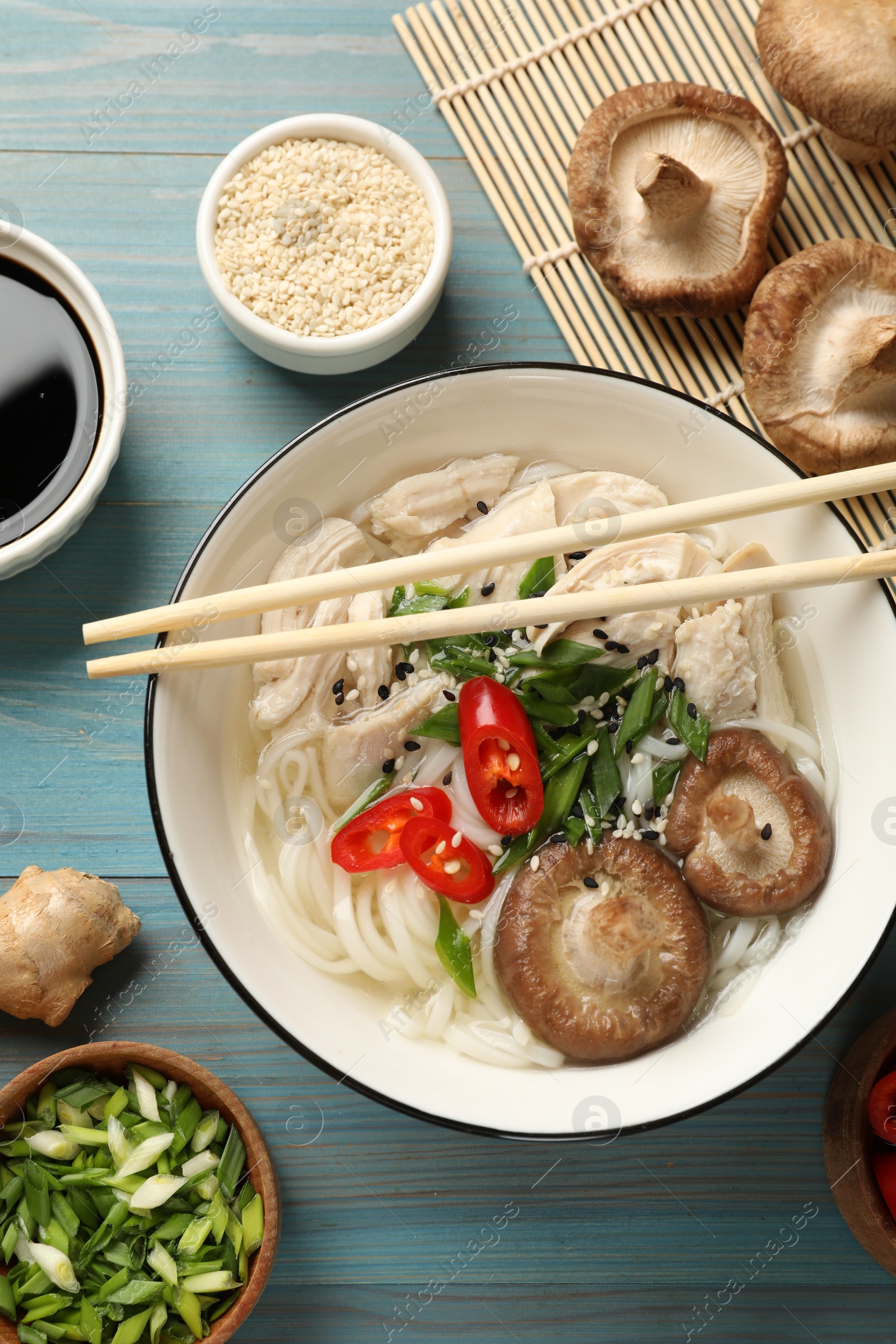 Photo of Delicious ramen with meat and ingredients on light blue wooden table, flat lay. Noodle soup