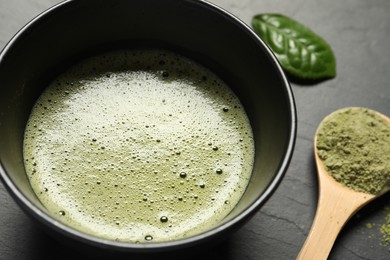 Photo of Cup of fresh matcha tea and bamboo spoon with green powder on black table, closeup